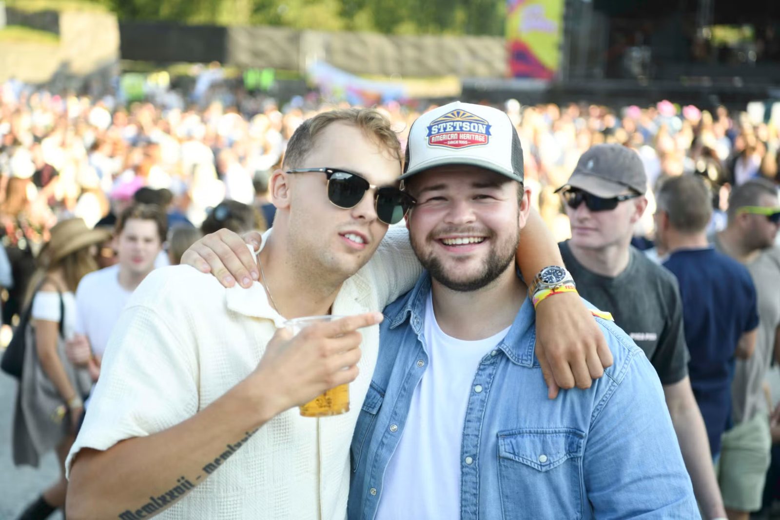 To kompiser med solbriller og caps i publikum
